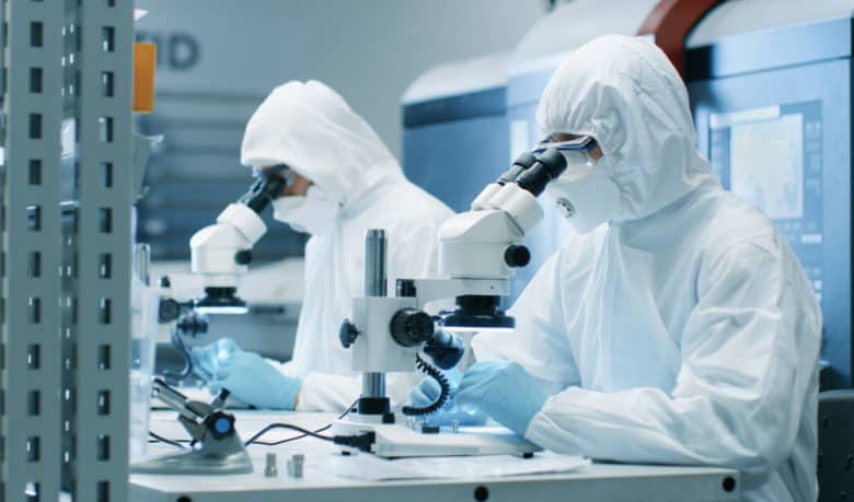 Scientists in cleanroom suits using microscopes in laboratory